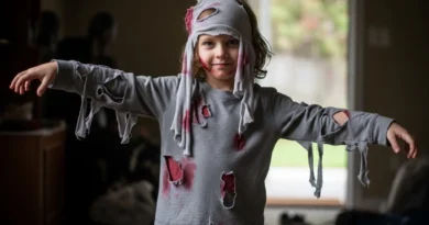 Dziecko w szarym, podartym stroju zombie z doczepionymi kawałkami materiału i sztuczną krwią.