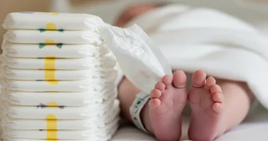 Stos pieluch obok noworodka w szpitalnej pościeli.