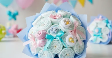 Bukiet na Baby Shower zrolowanych pieluch ozdobiony wstążkami, dziecięcymi skarpetkami i małą figurką w błękitnym papierze.