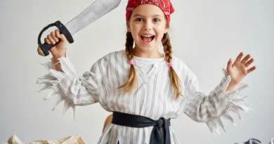 Dziewczynka w pirackim stroju DIY, z czerwoną chustką i tekturową szablą, radośnie pozuje przy stole z akcesoriami do szycia.