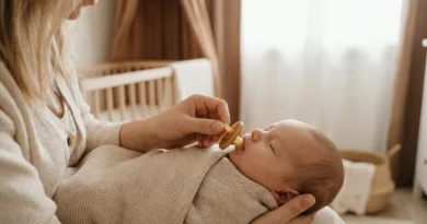 Kobieta delikatnie podaje kauczukowy smoczek noworodkowi owiniętemu w kocyk.