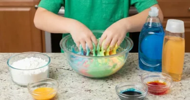 Dziecko mieszające dłońmi kolorowy slime w misce obok mąki, płynu do naczyń i barwników.