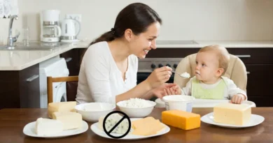 Kobieta karmi niemowlę przy stole z serami. Ser pleśniowy na pierwszym planie jest przekreślony znakiem zakazu.