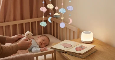 Śpiące niemowlę pod karuzelą z rysunkami mózgów. Obok leży otwarta książka anatomiczna i świecąca lampka.